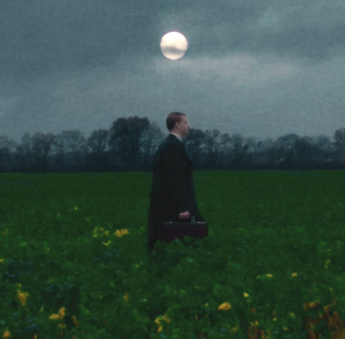 Figure crossing a field at dusk under a low moon, carrying a case